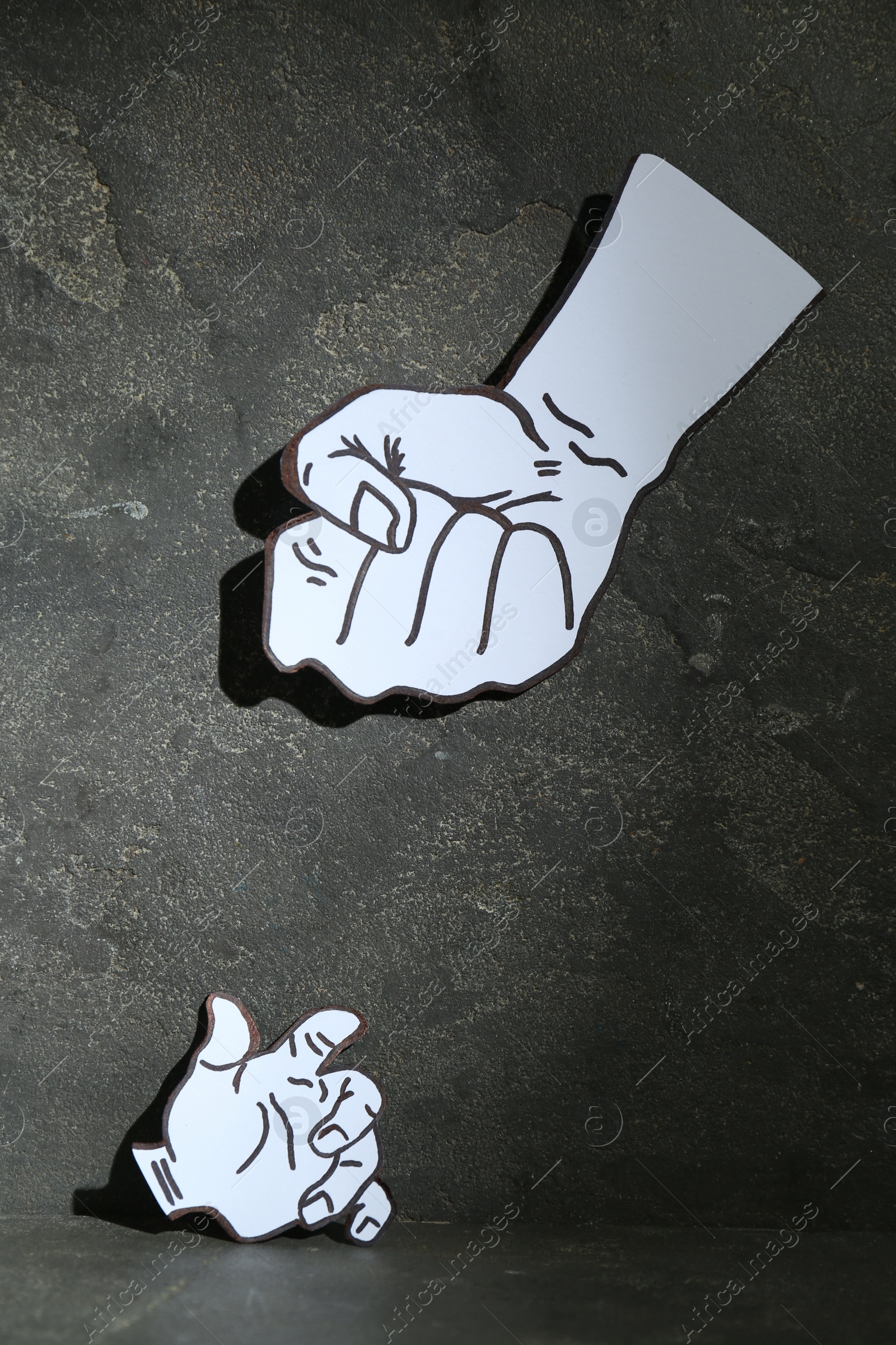 Photo of Stop child abuse. Paper cutout in shape of parent's fist above kid's hand on grey textured background