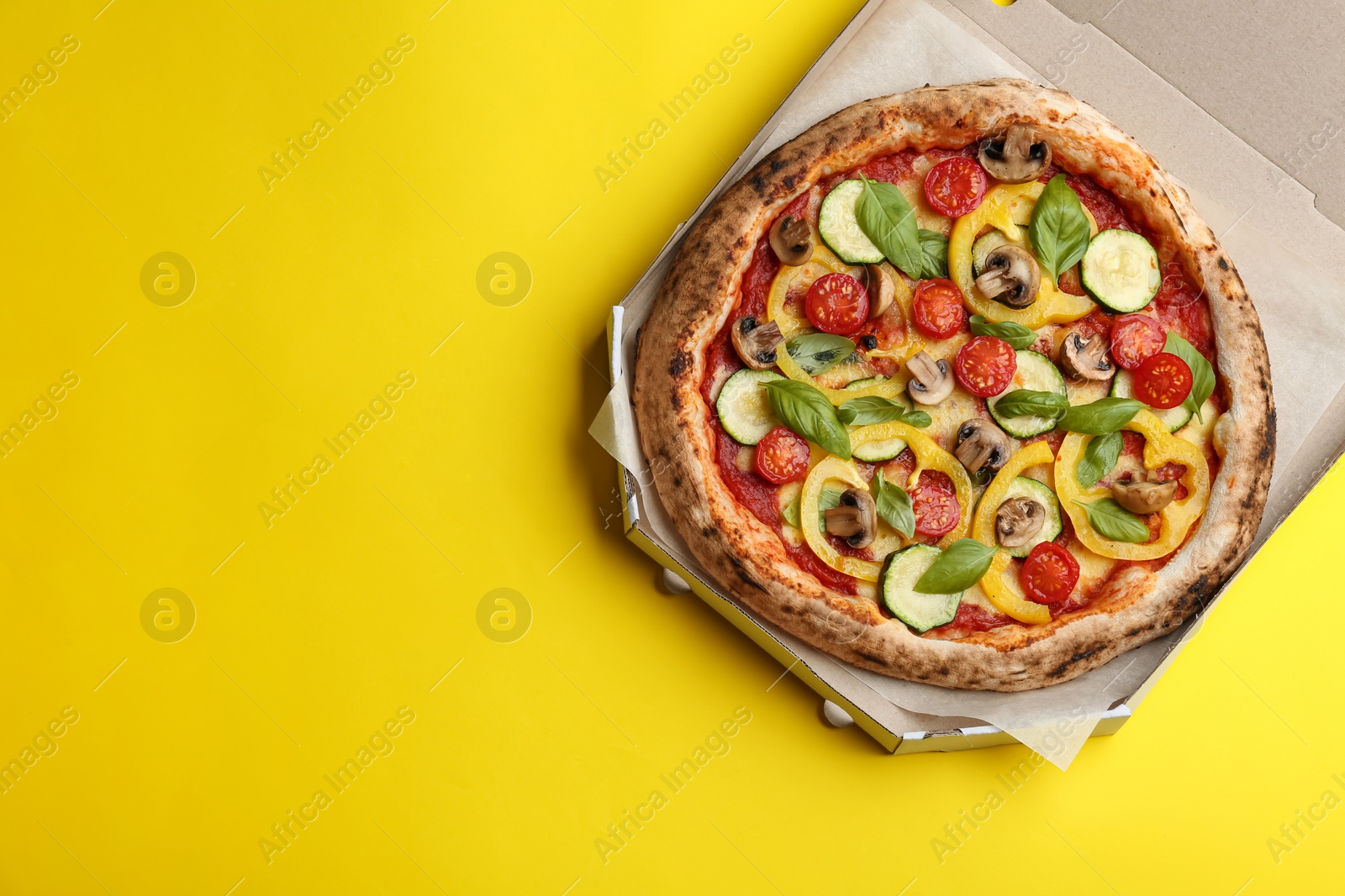 Photo of Delicious vegetable pizza in cardboard box on yellow background, top view. Space for text