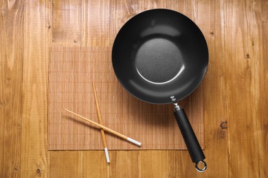 Photo of Empty iron wok and chopsticks on wooden table, top view