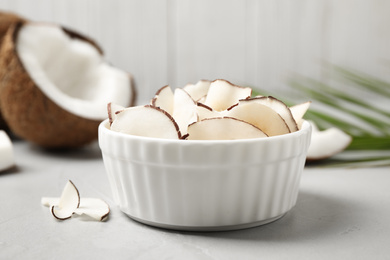 Tasty coconut chips on grey table against wooden background