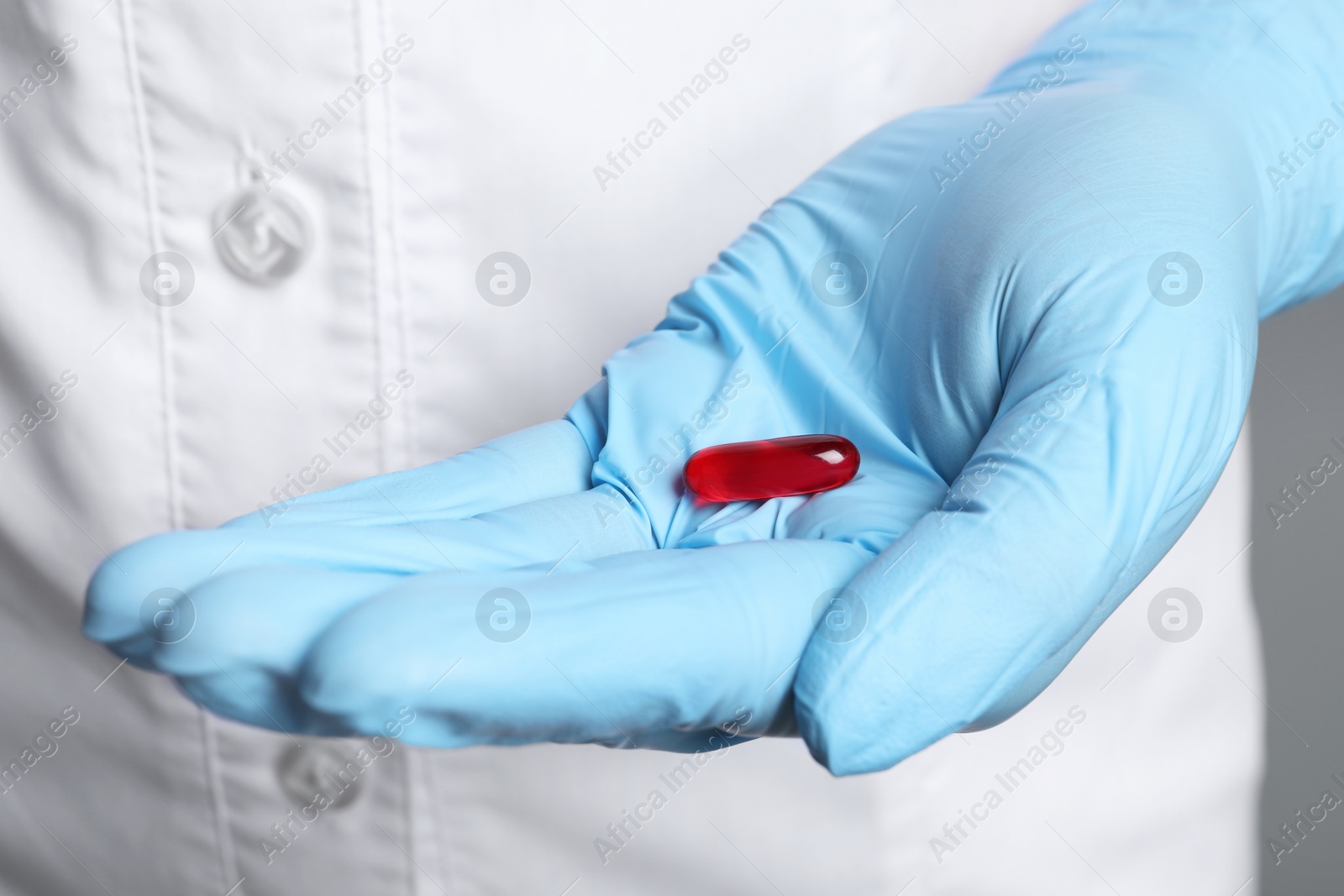 Photo of Doctor in medical glove holding pill on grey background, closeup