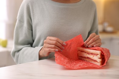 Photo of Woman packing sandwich into beeswax food wrap at light table in kitchen, closeup