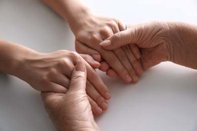 Photo of Young and elderly women holding hands together at white table, closeup