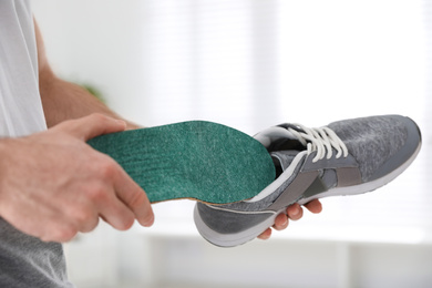 Photo of Man putting orthopedic insole into shoe at home, closeup