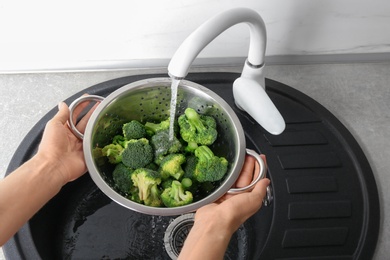 Photo of Woman washing fresh green broccoli in metal colander under tap water, closeup view