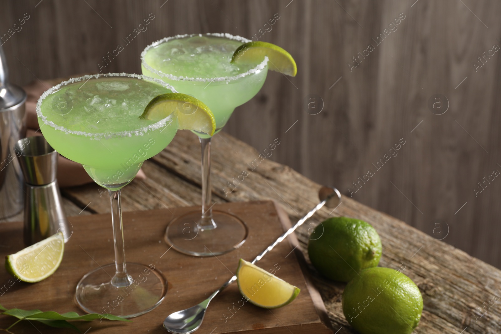 Photo of Delicious Margarita cocktail in glasses, limes and bartender equipment on wooden table