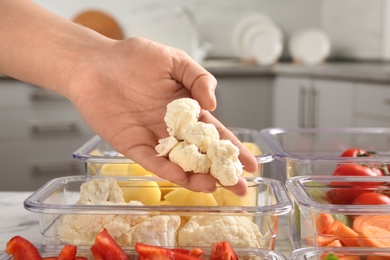Photo of Woman putting cut cauliflower into box and containers with raw vegetables in kitchen, closeup