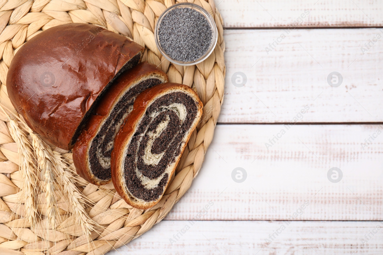 Photo of Cut poppy seed roll and spikelets on white wooden table, top view with space for text. Tasty cake