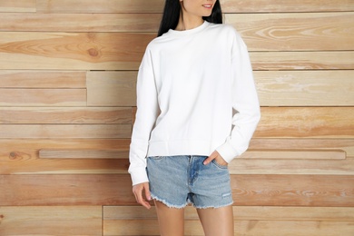 Photo of Young woman in sweater at wooden wall, closeup. Mock up for design