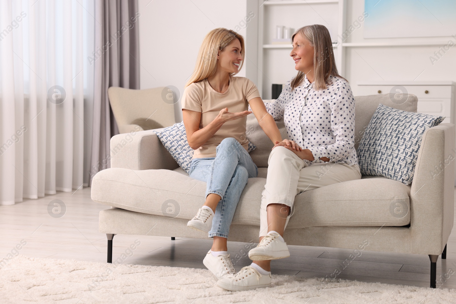 Photo of Happy mature mother and her daughter talking on sofa at home