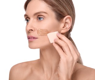 Woman applying foundation on face with makeup sponge against white background