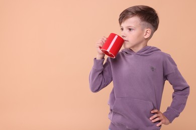 Photo of Cute boy drinking beverage from red ceramic mug on beige background, space for text