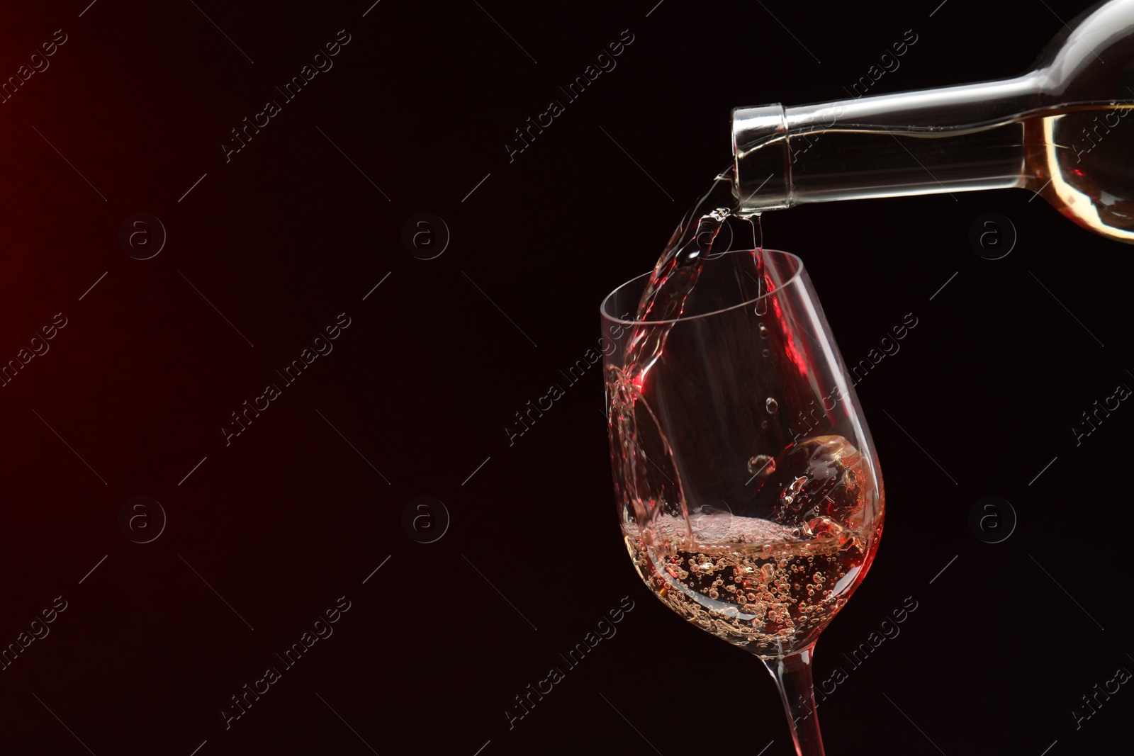 Photo of Pouring white wine from bottle into glass on dark background, space for text