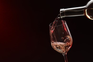 Photo of Pouring white wine from bottle into glass on dark background, space for text