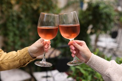 Photo of Women clinking glasses with rose wine outdoors, closeup