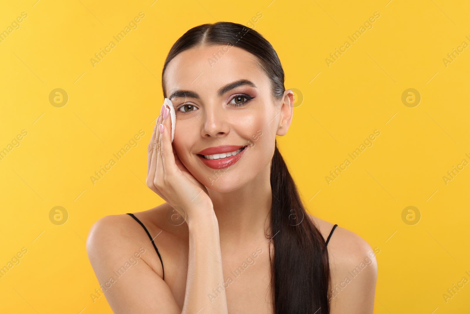 Photo of Beautiful woman removing makeup with cotton pad on orange background