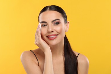 Beautiful woman removing makeup with cotton pad on orange background