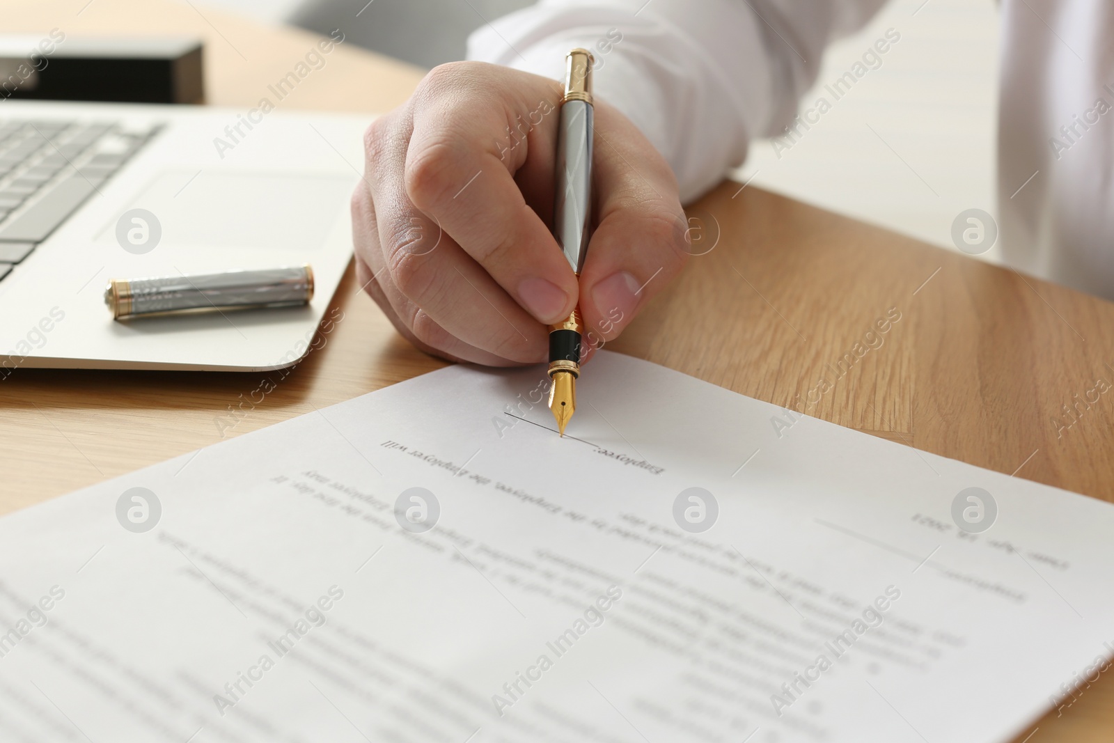 Photo of Notary signing document at wooden table, closeup