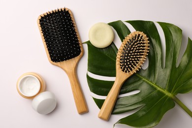 Wooden hairbrushes, cosmetic products and green leaf on white background, flat lay