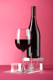 Photo of Stylish presentation of delicious red wine in bottle and glass on pink background