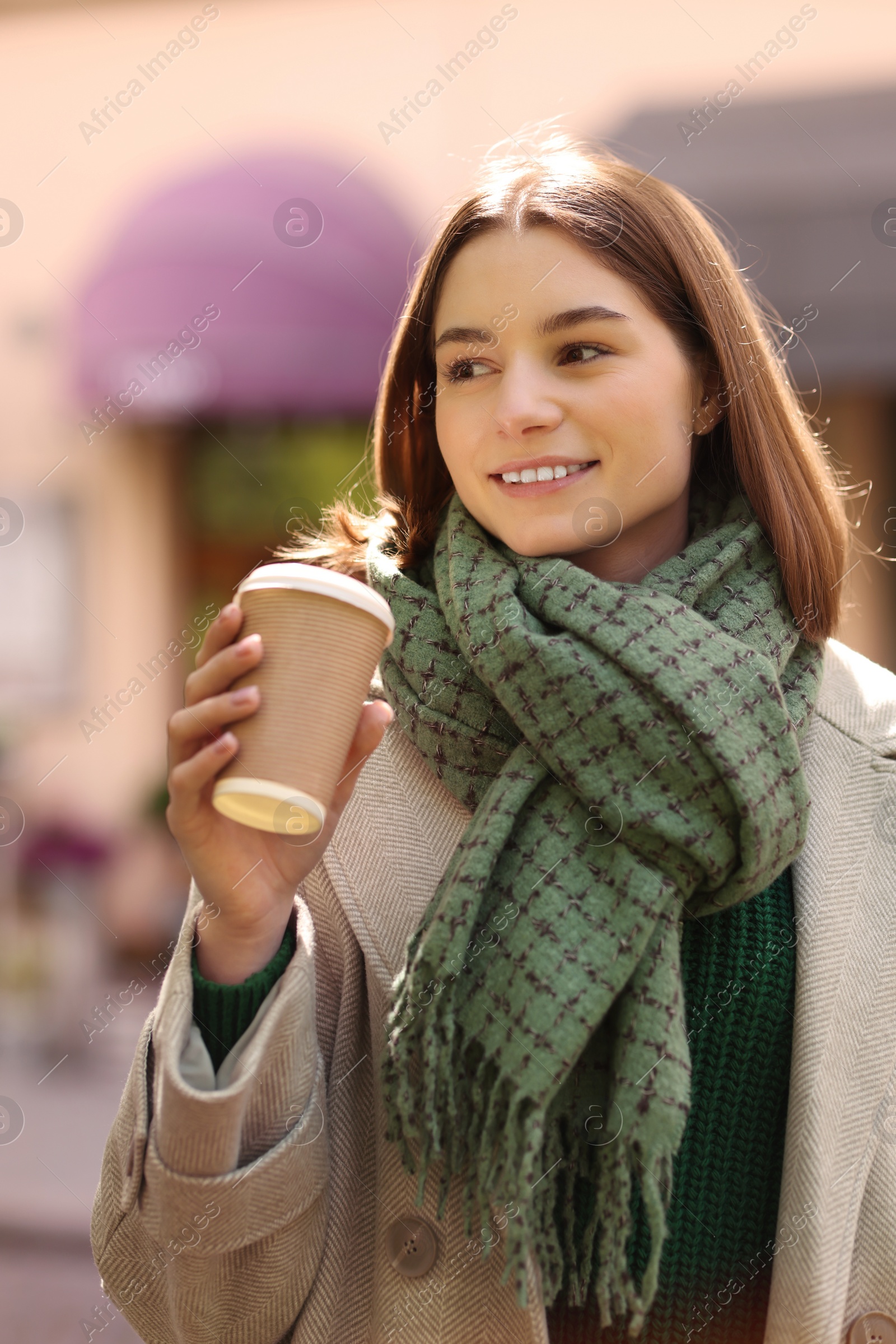 Photo of Beautiful woman in warm scarf with paper cup of coffee on city street