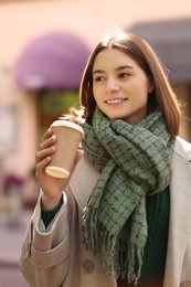 Photo of Beautiful woman in warm scarf with paper cup of coffee on city street