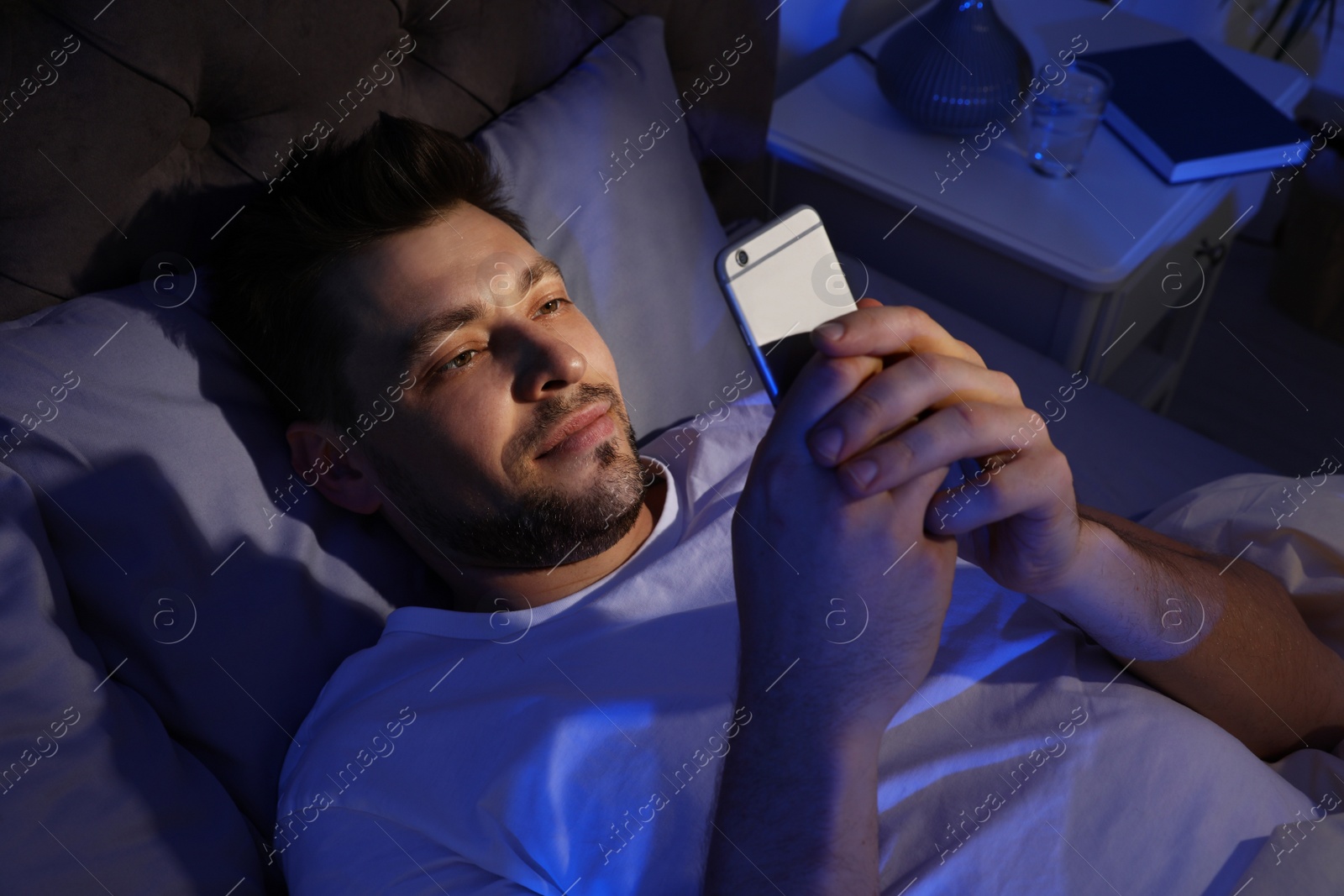 Photo of Handsome man using smartphone in dark room at night. Bedtime