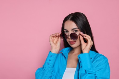 Photo of Attractive serious woman wearing fashionable sunglasses against pink background. Space for text