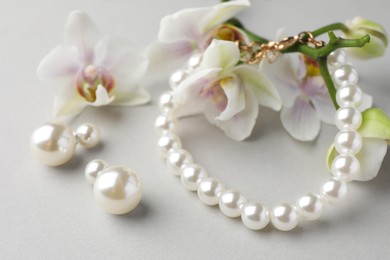 Photo of Elegant pearl earrings, bracelet and orchid flowers on white background, closeup