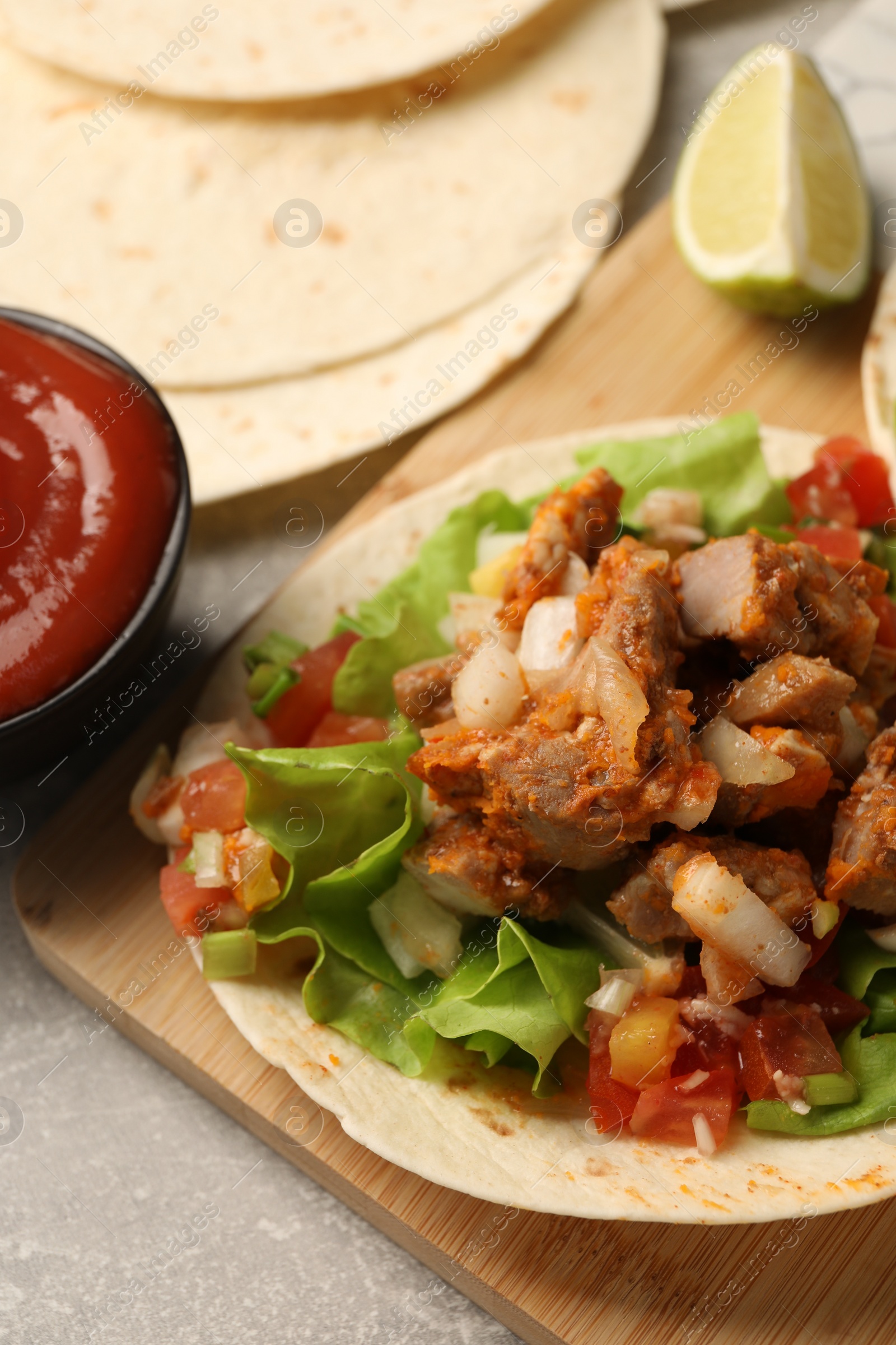 Photo of Delicious tacos with vegetables and meat on grey textured table, closeup