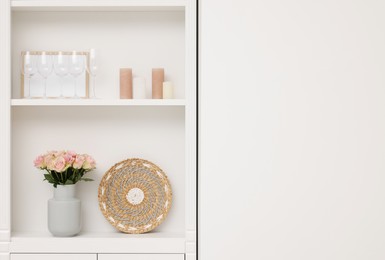 Shelves with different decor near white wall, space for text. Interior design