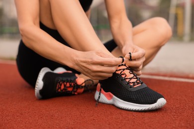 Woman tying shoelaces before training outdoors, closeup