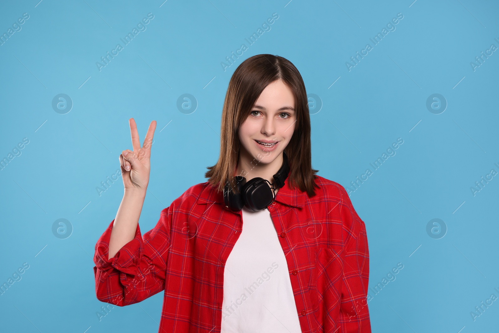 Photo of Portrait of teenage girl showing peace gesture on light blue background