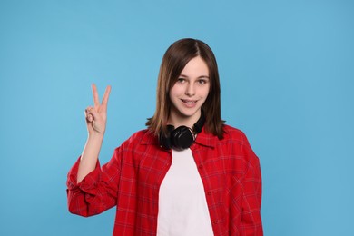 Photo of Portraitteenage girl showing peace gesture on light blue background
