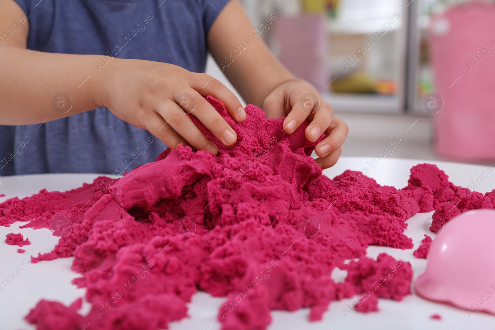 Photo of Little girl playing with bright kinetic sand at table indoors, closeup