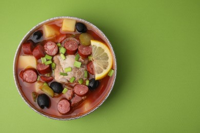 Photo of Meat solyanka soup with thin dry smoked sausages in bowl on light green background, top view. Space for text