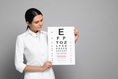 Photo of Ophthalmologist with vision test chart on gray background, space for text