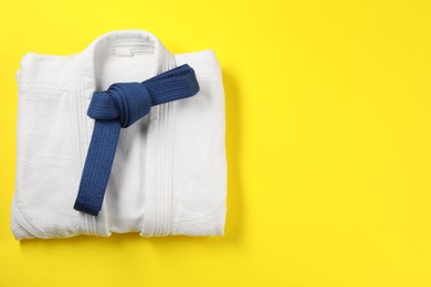 Photo of Blue karate belt and white kimono on yellow background, top view. Space for text