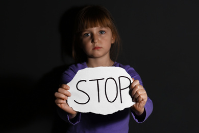 Abused little girl with sign STOP near black wall. Domestic violence concept