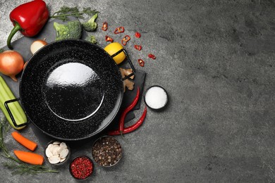 Empty iron wok and raw ingredients on grey table, flat lay. Space for text