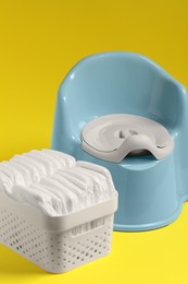 Photo of Light blue baby potty and diapers on yellow background. Toilet training