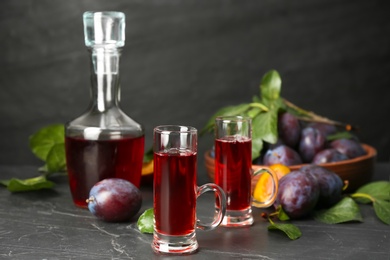 Photo of Delicious plum liquor and ripe fruits on black table. Homemade strong alcoholic beverage