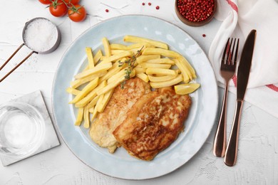 Tasty soda water battered fish, potato chips and lemon slice served on white textured table, flat lay