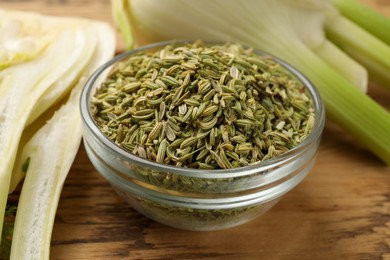 Photo of Fennel seeds in bowl and fresh vegetables on wooden table, closeup