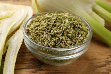 Fennel seeds in bowl and fresh vegetables on wooden table, closeup