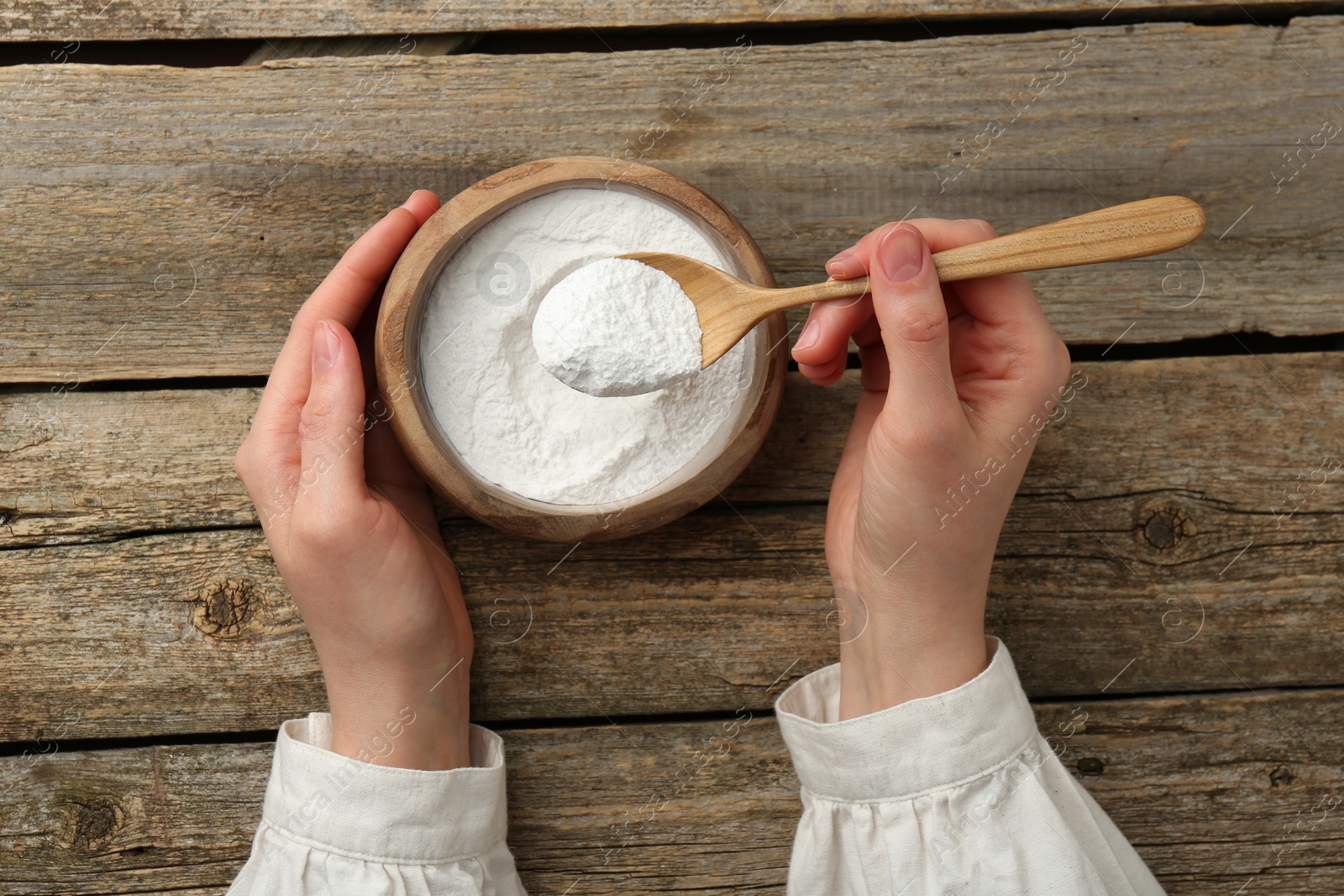 Photo of Woman taking baking powder with spoon from bowl at wooden table, top view