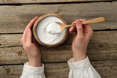 Photo of Woman taking baking powder with spoon from bowl at wooden table, top view