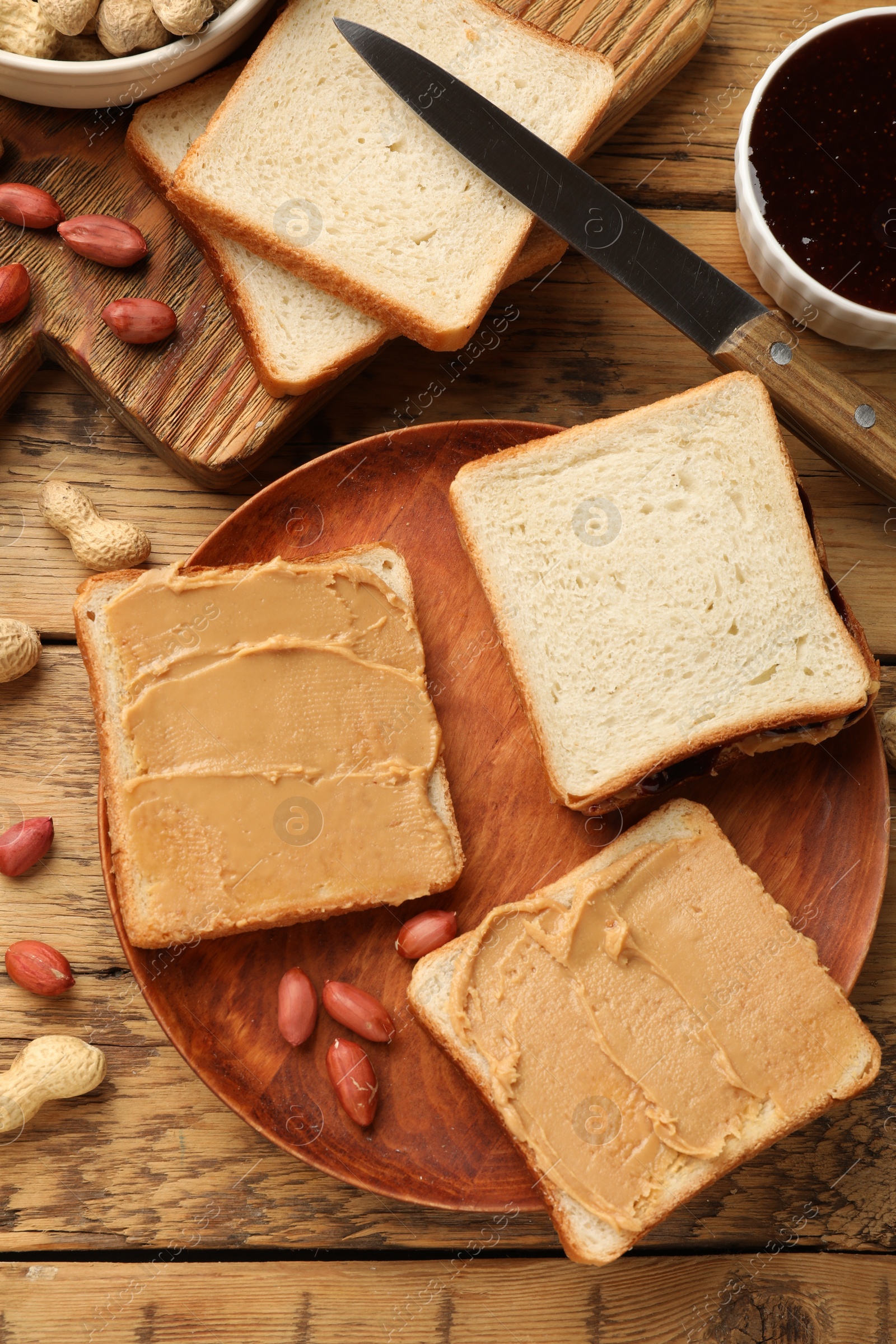 Photo of Tasty peanut butter sandwiches and peanuts on wooden table, flat lay