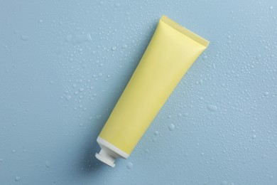 Moisturizing cream in tube on light blue background with water drops, top view