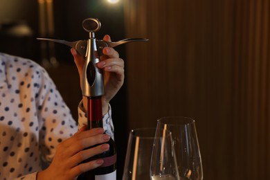 Photo of Romantic dinner. Woman opening wine bottle with corkscrew indoors, closeup and space for text